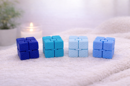 Four blue and light blue puzzle cube toys on a textured surface with a blurred candle and plant in the background.