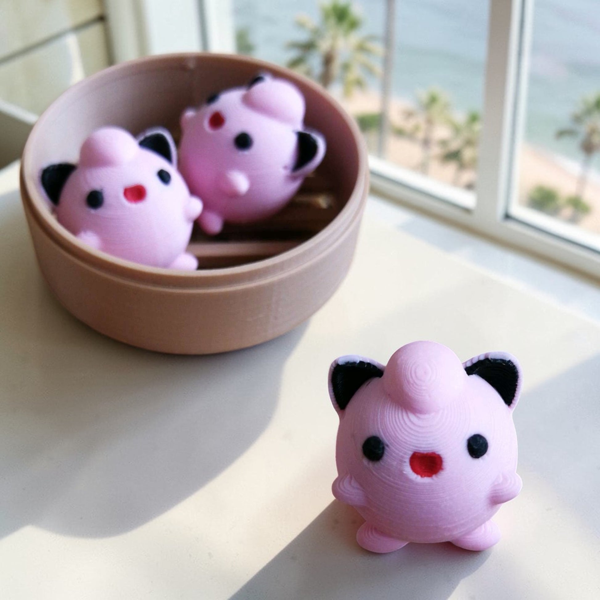 Pink jigglypuff toys on a light surface with a bowl and window view.