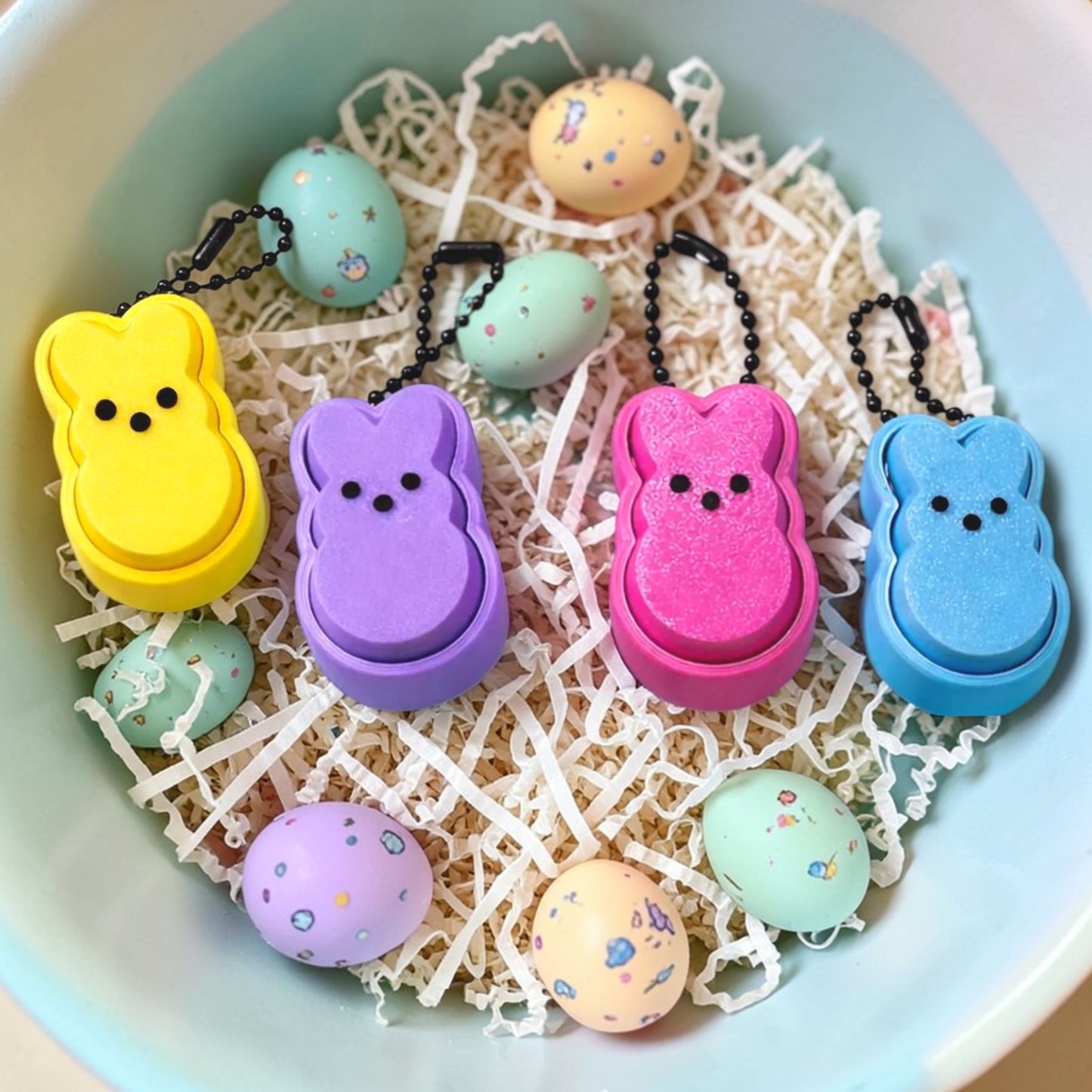 Colorful Peep-shaped keychains on a textured surface with small pastel-colored eggs.