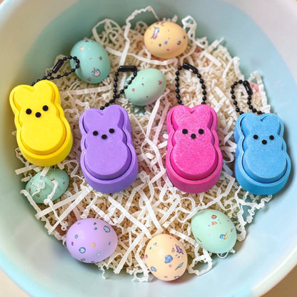 Colorful Peep-shaped keychains on a textured surface with small pastel-colored eggs.