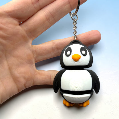 Penguin-shaped keychain held in a hand against a light blue background