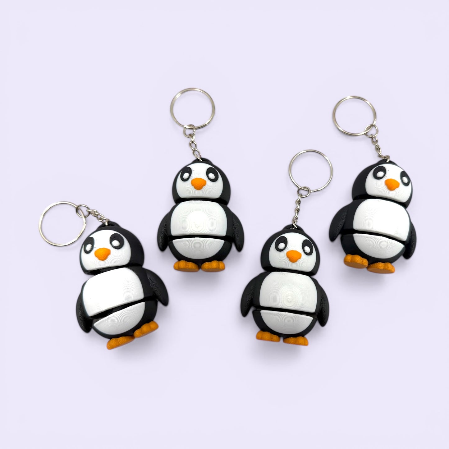 Four penguin-shaped keychains on a light purple background